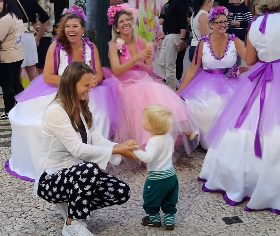 15-month-old toddler dancing and making people laugh at the Madeira Flower Festival, surrounded by women in traditional flower dresses