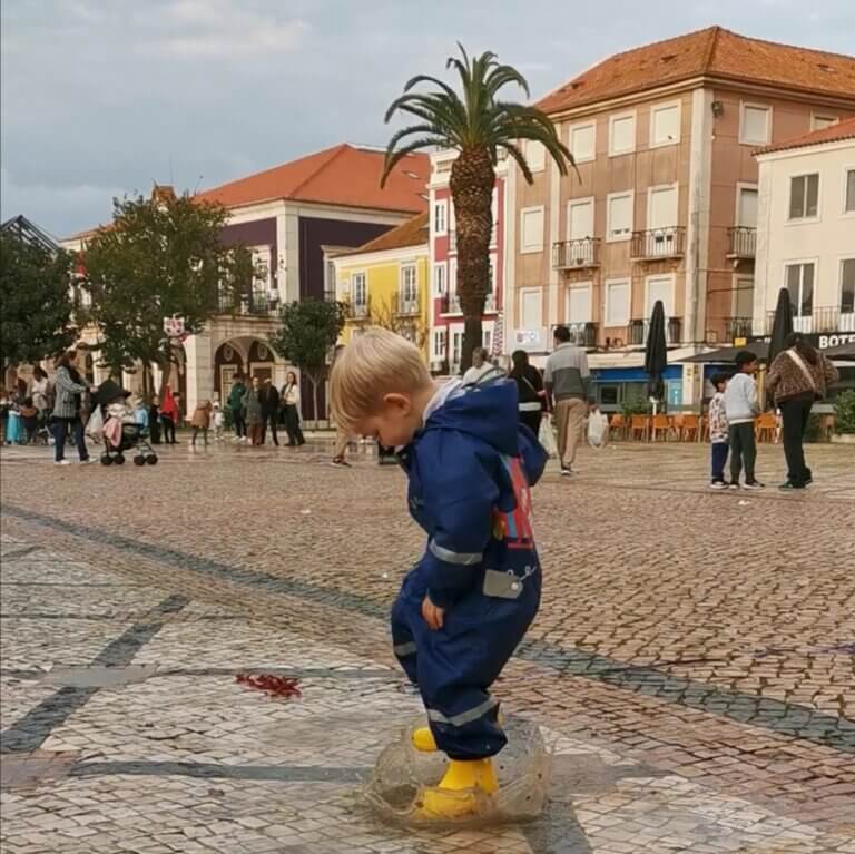 Child in a yellow rain suit jumping into puddles in a city square — embracing joy, freedom, and sensory engagement through play