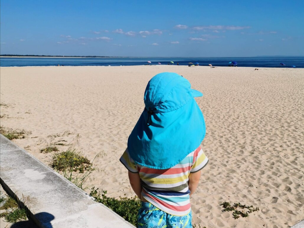 A toddler stands facing an empty beach and open sky, symbolizing how boredom and stillness create space for raising creative kids through sustainable, harm-free practices.